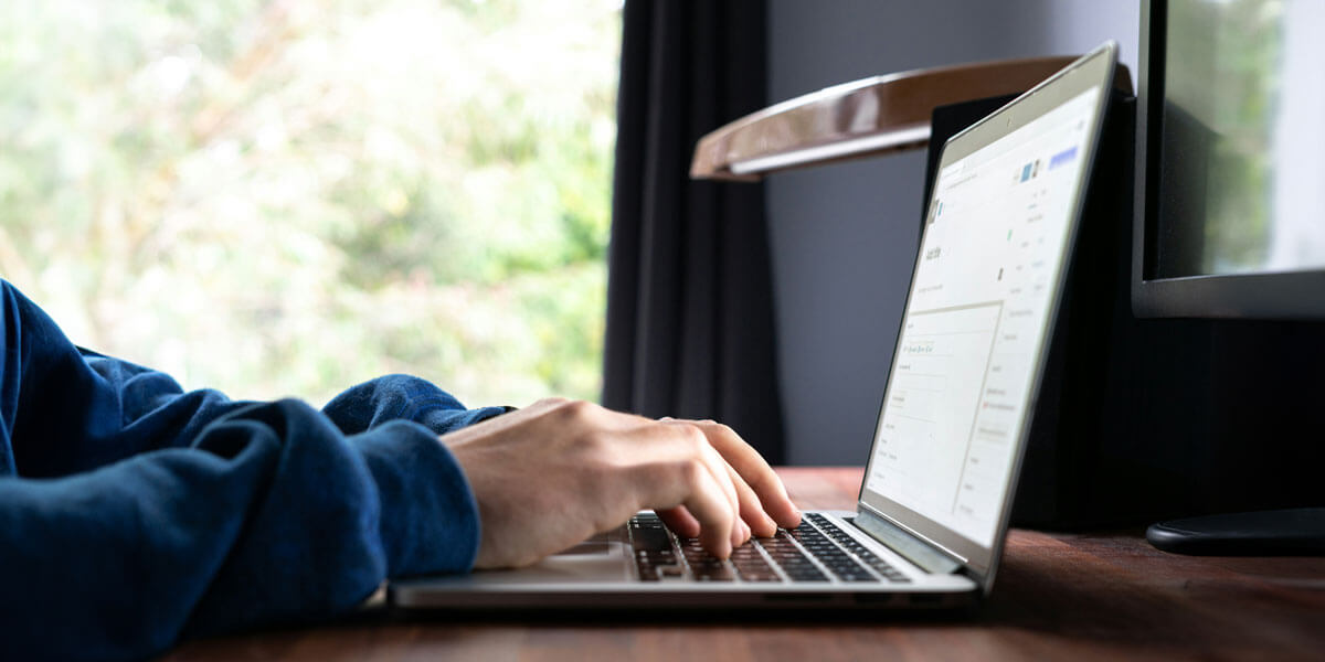 A person focused on typing on a laptop computer, with hands positioned on the keyboard and screen illuminated.