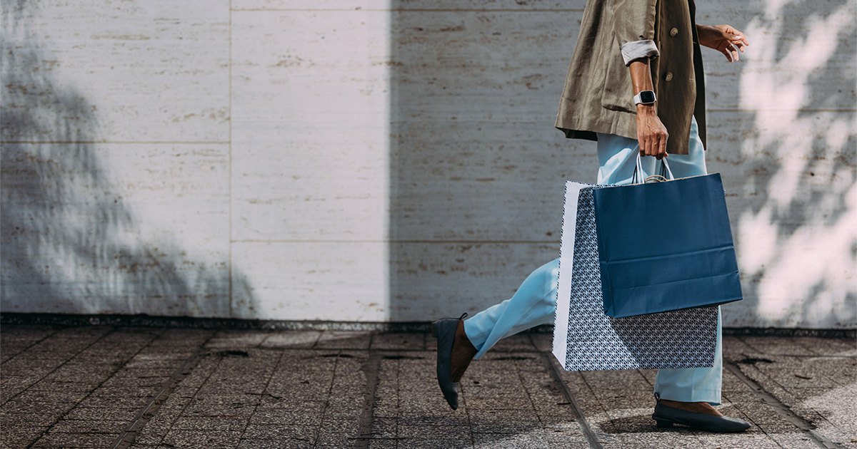 person walking down sidewalk and holding shopping bags