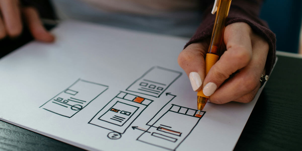 A person sketching a website wireframe on paper, using a pen to highlight interface elements and navigation paths.